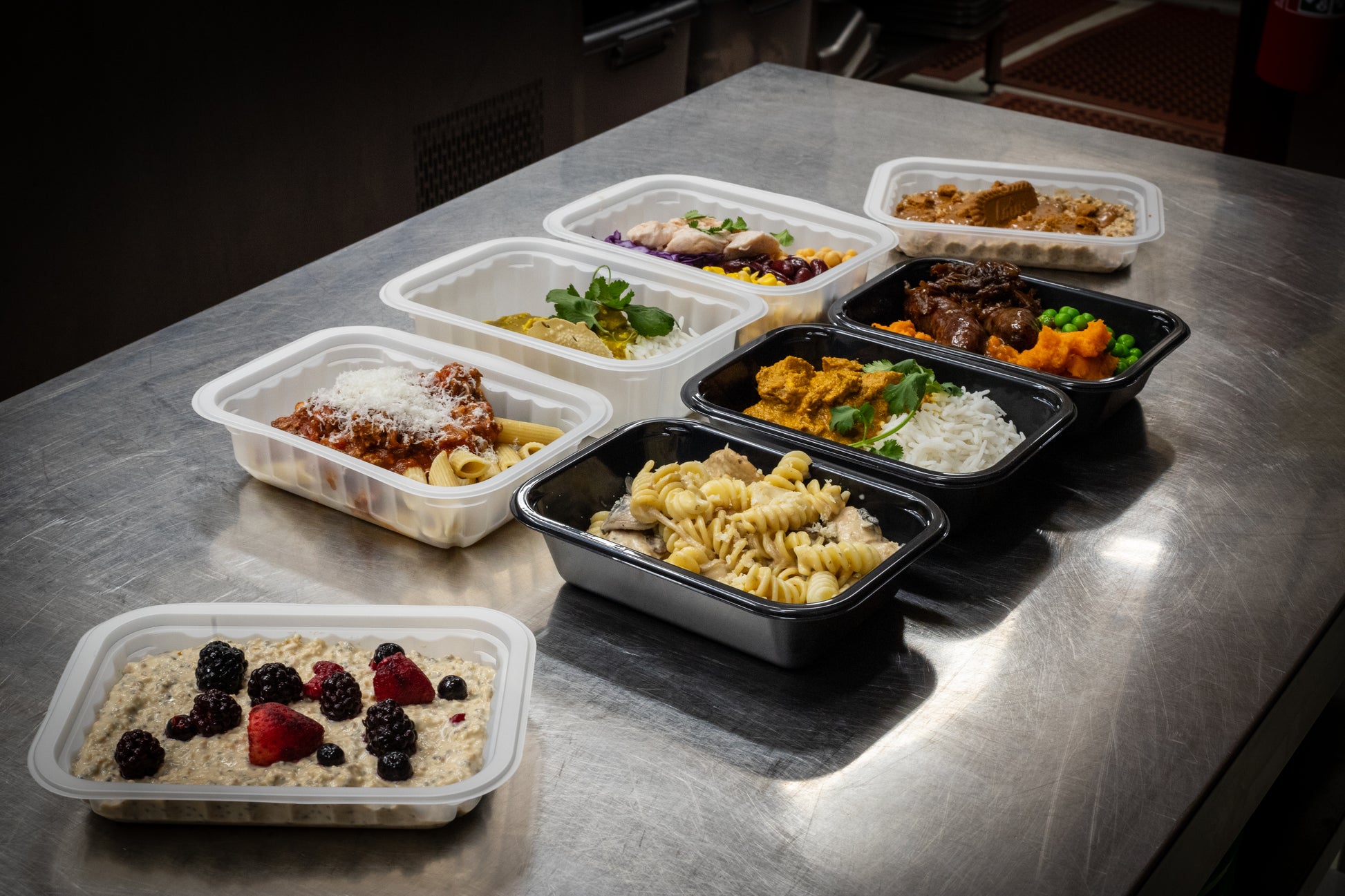Chef-prepared high-protein ready meals from Fuel & Prep Co arranged on a prep table, including pasta, rice and breakfast meals.